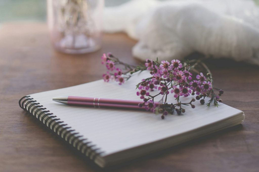 A journal with a fuchsia pen and small pink flowers sitting atop the open page.