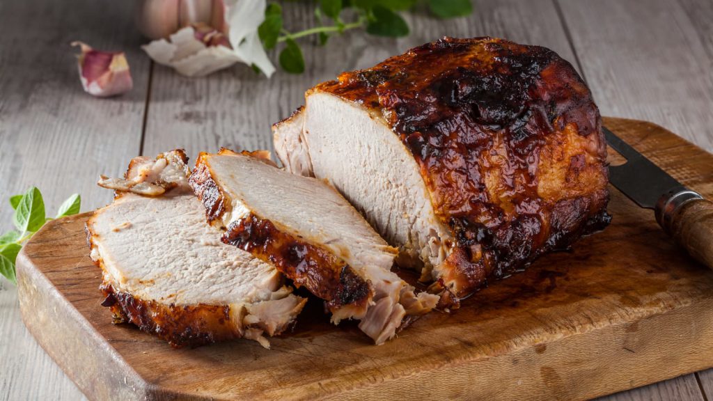 Wooden cutting board with a cooked, sliced pork roast sitting atop it
