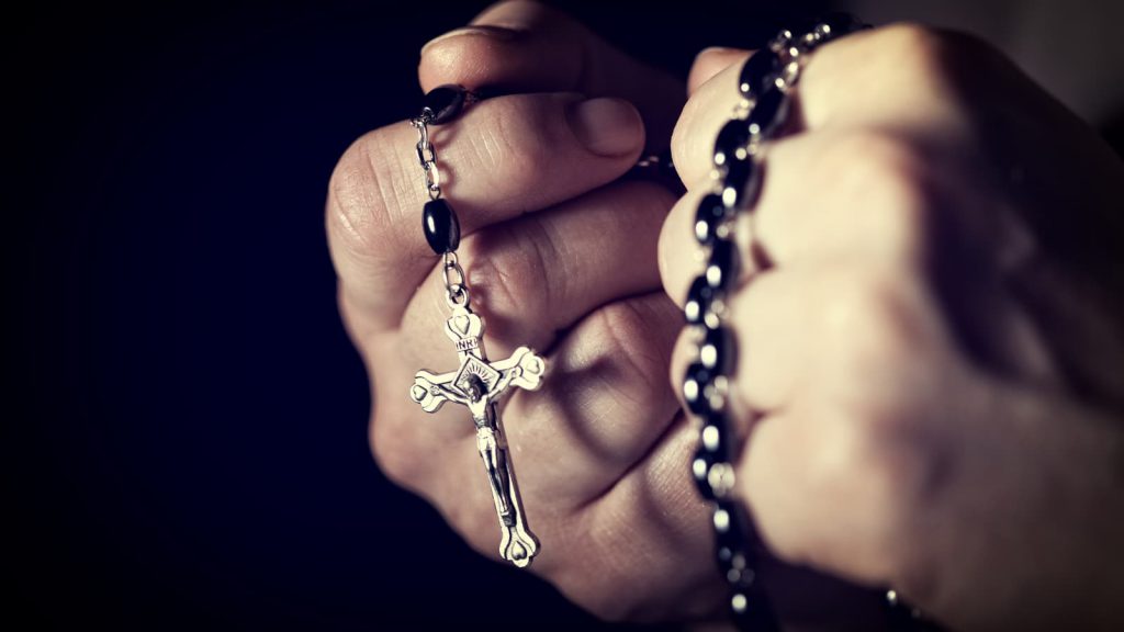 Folded hands holding a Rosary
