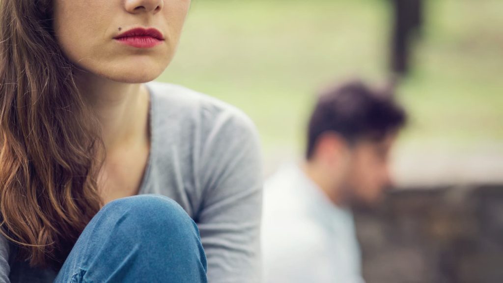 Closeup of sad woman's face with her spouse blurred in the background